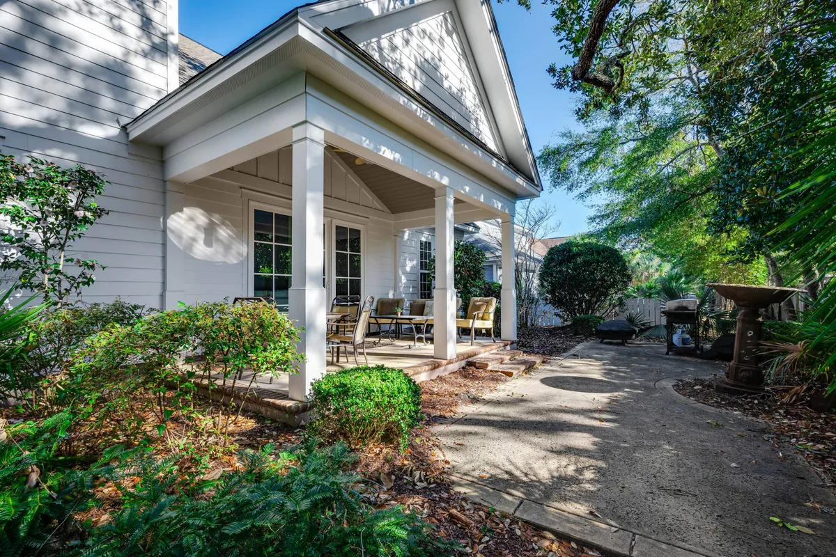 A tranquil exterior view of a covered porch surrounded by lush greenery, featuring a dining set and a decorative fountain. This space invites guests to enjoy meals outdoors, relax, or gather together in a scenic backyard setting. The welcoming vibe makes it perfect for family barbecues and shared moments.