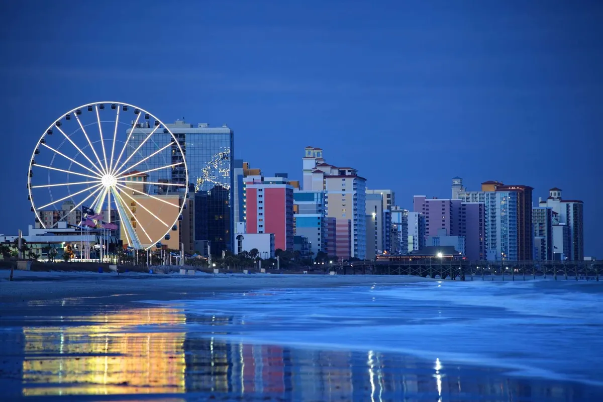 A cheerful exterior shot highlighting a Ferris wheel against a backdrop of the ocean, colorful buildings, and gentle waves. The scene is bustling with activity, capturing the energy of nearby attractions and the easy beach access suggested in the section. It evokes a sense of playfulness and adventure right by the shoreline.