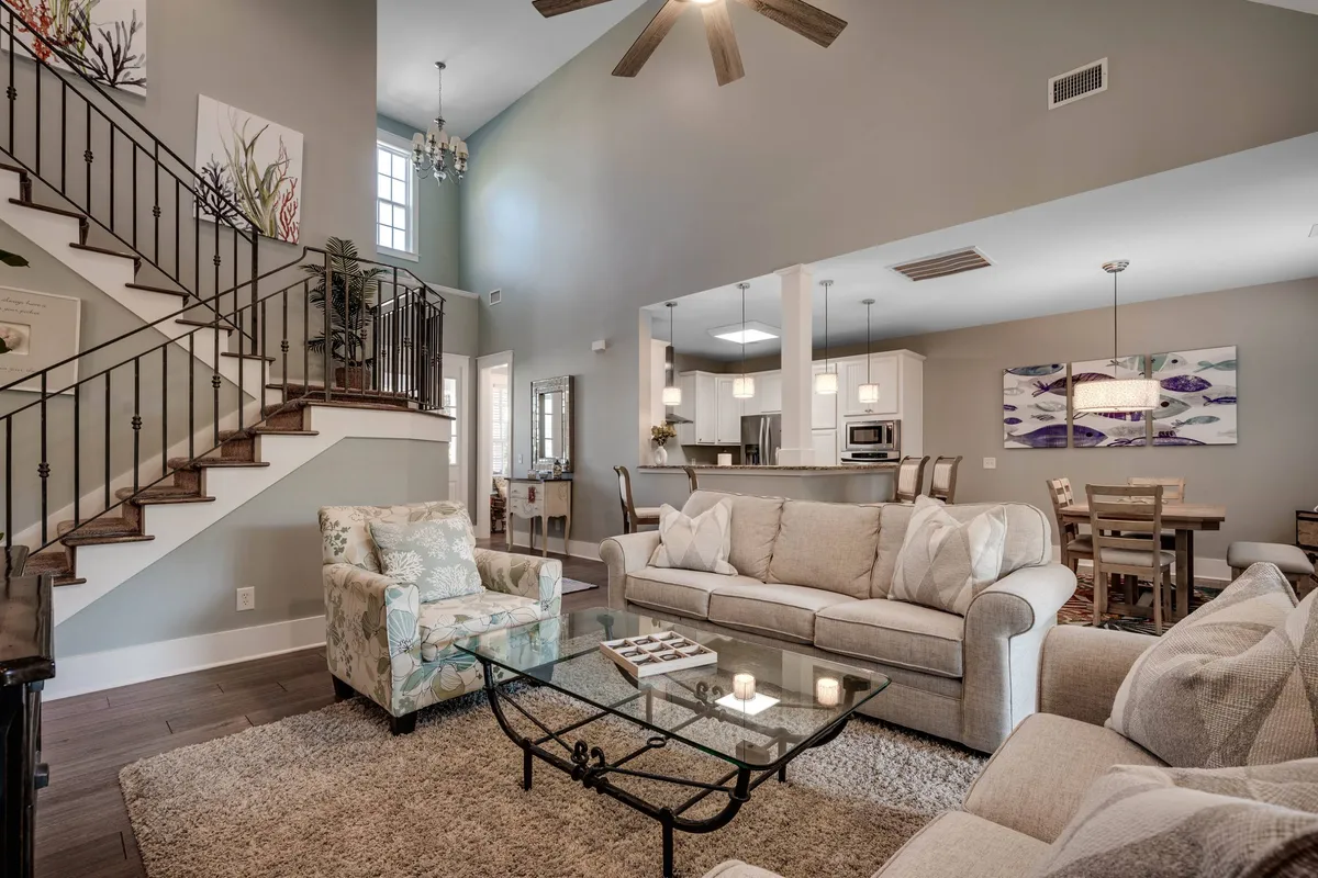 A cozy living room scene featuring a plush sofa, a glass coffee table, and a view extending toward the dining area. Modern light fixtures and a staircase add character, while the space exudes a sense of warmth and casual elegance. The layout visually connects the living and dining areas, reinforcing the open-concept theme.