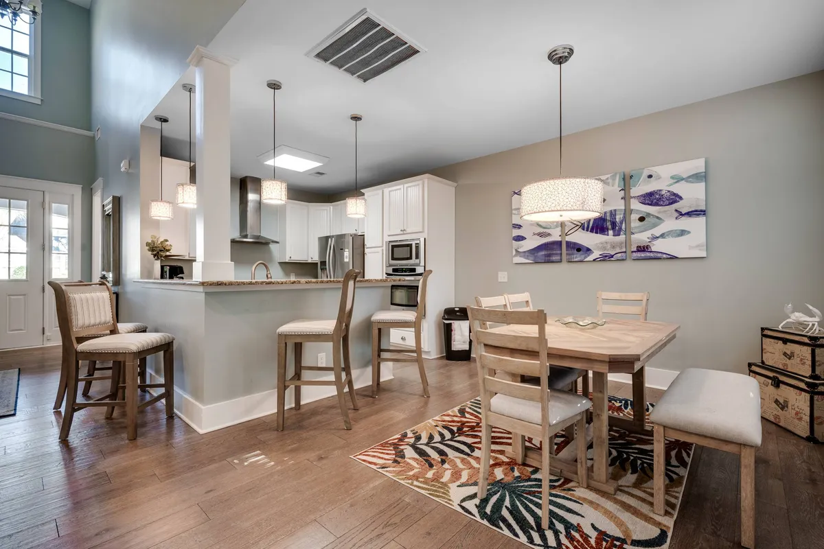 A modern, welcoming dining area with a central table surrounded by bar stools and chairs. A kitchen island is visible, along with vibrant artwork on the wall. The space is designed for social gatherings, meals, and entertainment, capturing the experience of coming together over food.