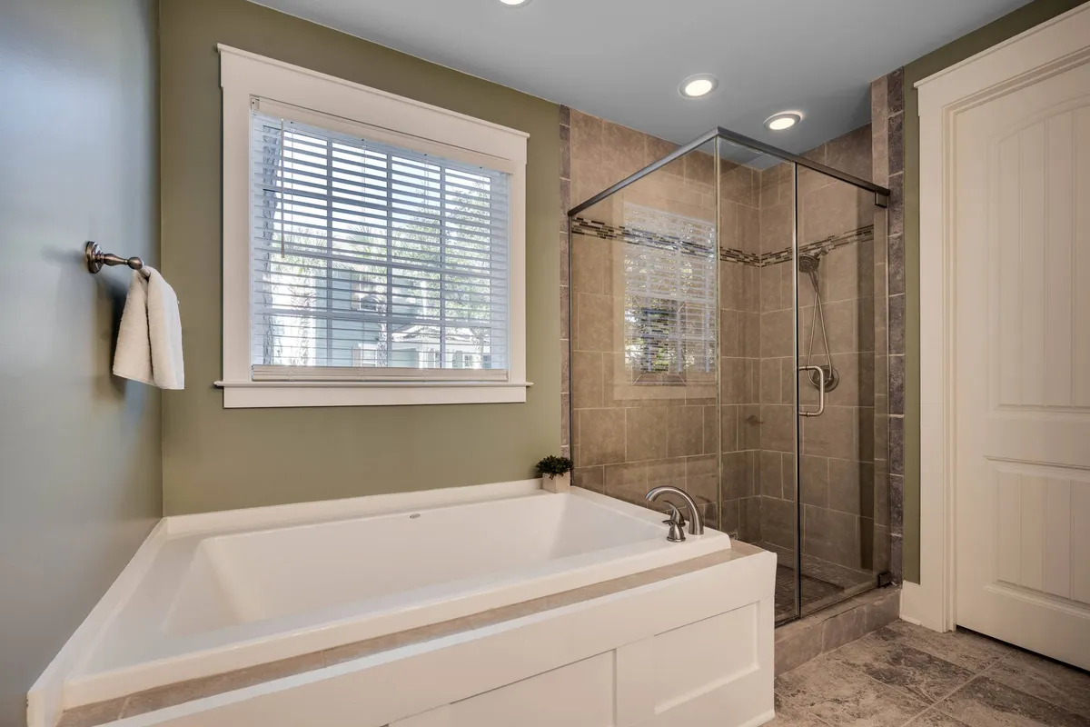 A tranquil bathroom featuring a deep soaking bathtub, a separate shower enclosure, and a window that lets in soft, natural light. The serene ambiance makes it ideal for unwinding after a day at the pool or exploring the resort.