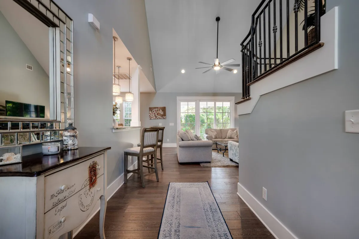 A view from the entryway that seamlessly leads to an open living area filled with natural light from large windows. A wooden console table and a mirror by the entrance add warmth, while the inviting living space beyond features cozy furniture and a fireplace. The dining table is visible, suggesting easy flow between living and dining zones.