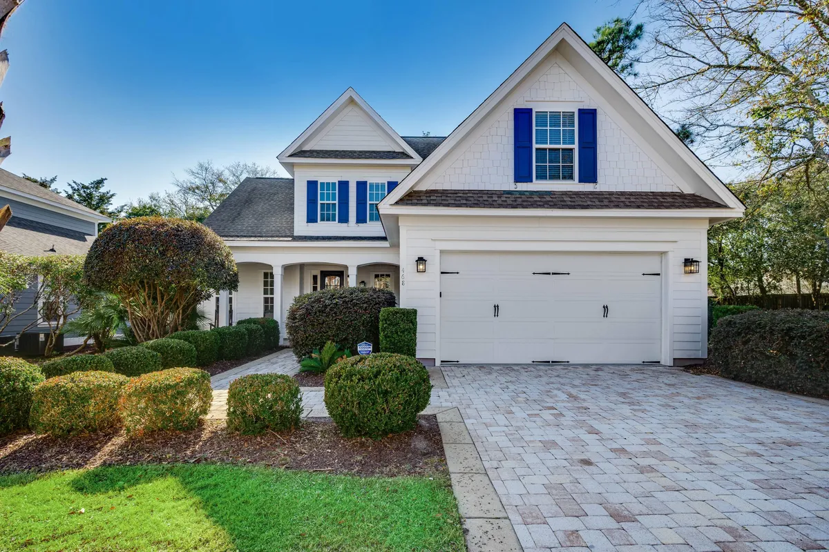 The image presents the home's front porch and a partial view of the garage, framed by a landscaped garden. The garage is clearly visible, indicating available parking, while the garden and porch add curb appeal and an inviting first impression.